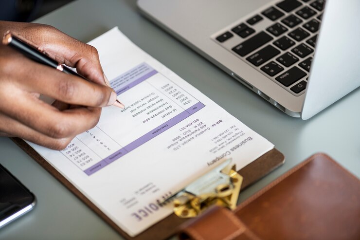 Person filling out a business invoice by hand next to a laptop